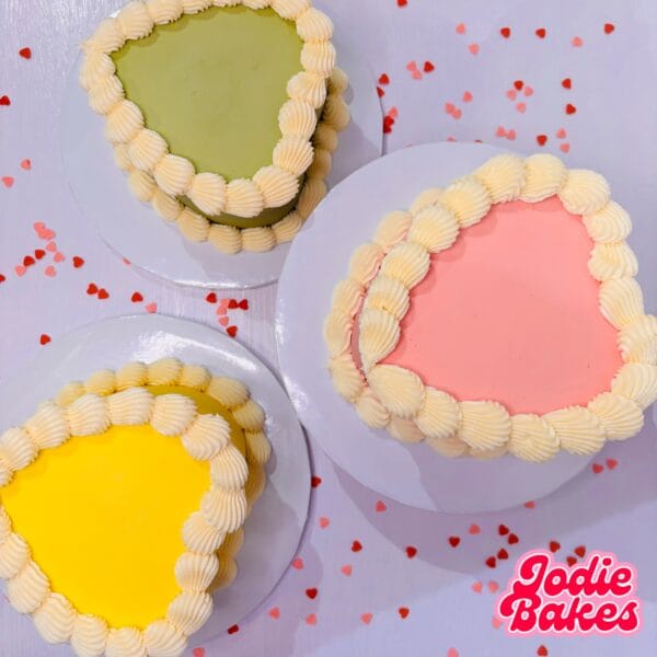 Three personalised heart cakes in green, lemon and pink with cream piping, by Jodie Bakes, Leeds