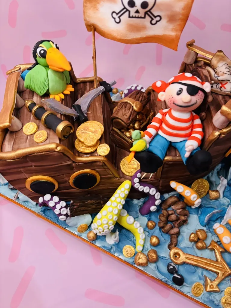 Pirate ship birthday cake with a parrot, pirate figure, treasure, gold coins and octopus tentacles, by Jodie Bakes, Leeds