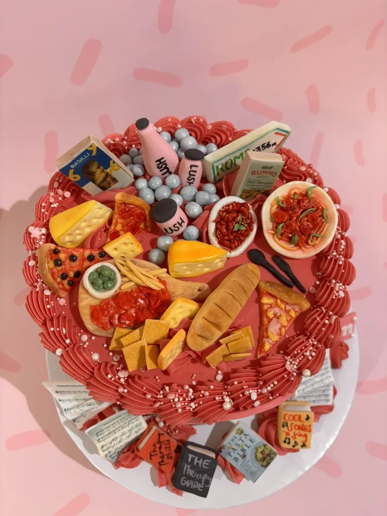 Red buttercream cake topped with a miniature sugar party food spread of pizza, cheese, bread and pasta, by Jodie Bakes, Leeds