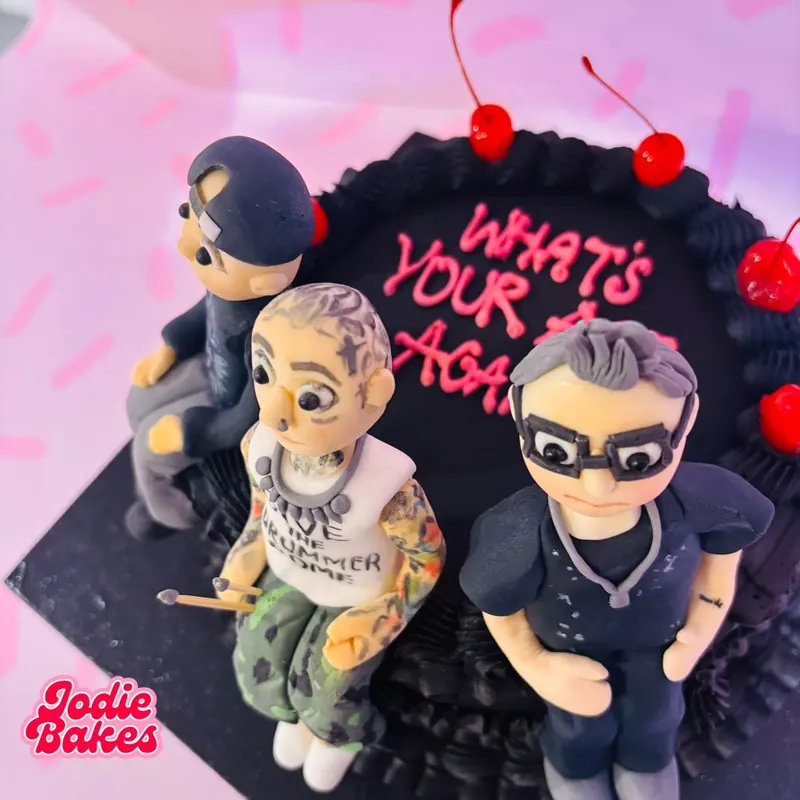 Black birthday cake with three handmade sugar figures, cherries and pink piped writing, by Jodie Bakes, Leeds